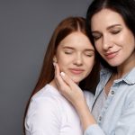 Mother and her teenage daughter on grey background. Space for text
