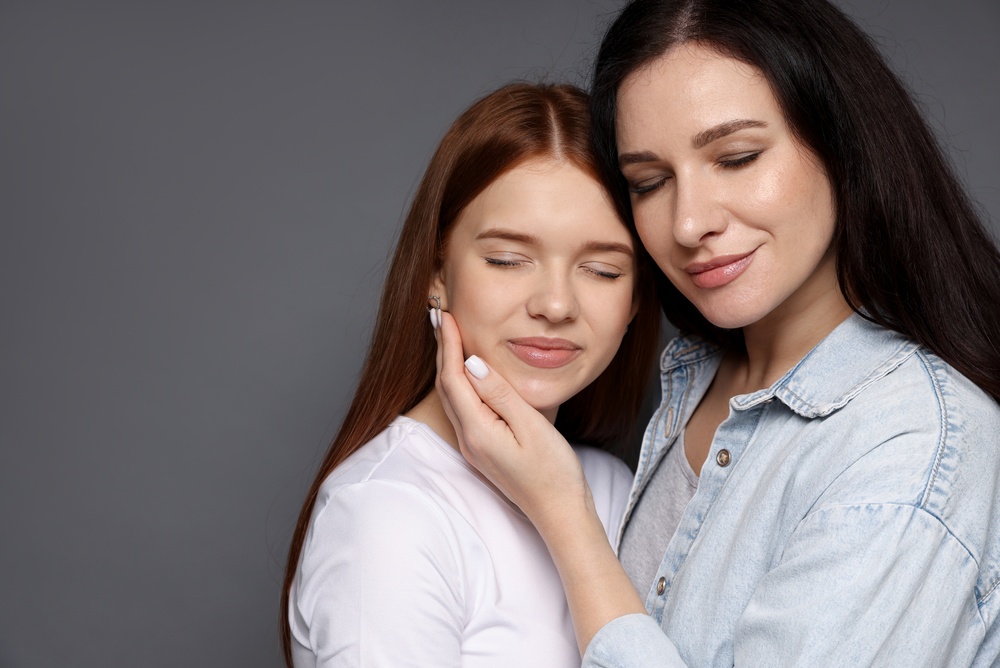 Mother and her teenage daughter on grey background. Space for text