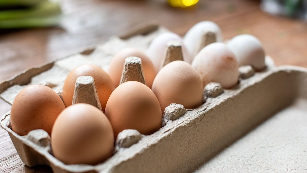 A close-up of a carton filled with brown and white eggs on a wooden table, showcasing natural variations in egg color and texture.