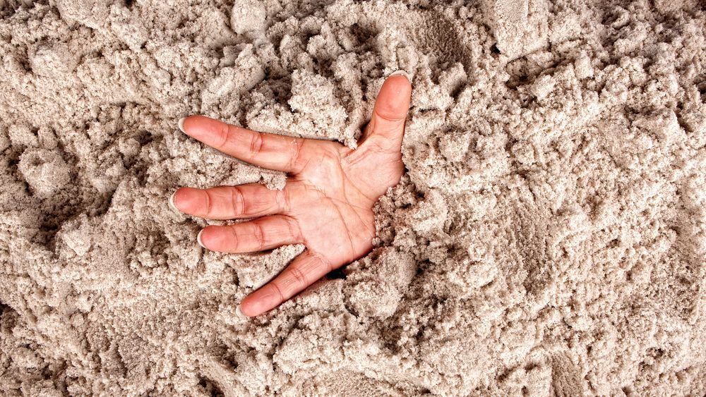 Hand on a beach sinking or drowning in quicksand