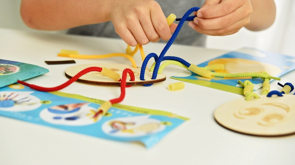 development of fine motor skills. Early education, Montessori Method. Cognitive skills, Children development. Close up of child hands playing with lace or rope and pasta