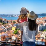 A tourist mother and her little daughter enjoy the view of the beautiful cityscape of Lisbon, with the colorful houses and roofs, Portugal