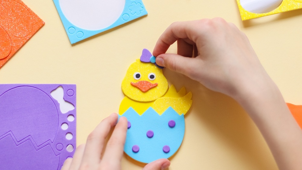 The hands of a caucasian teenage girl stick a lilac bow sticker on a yellow chicken felt