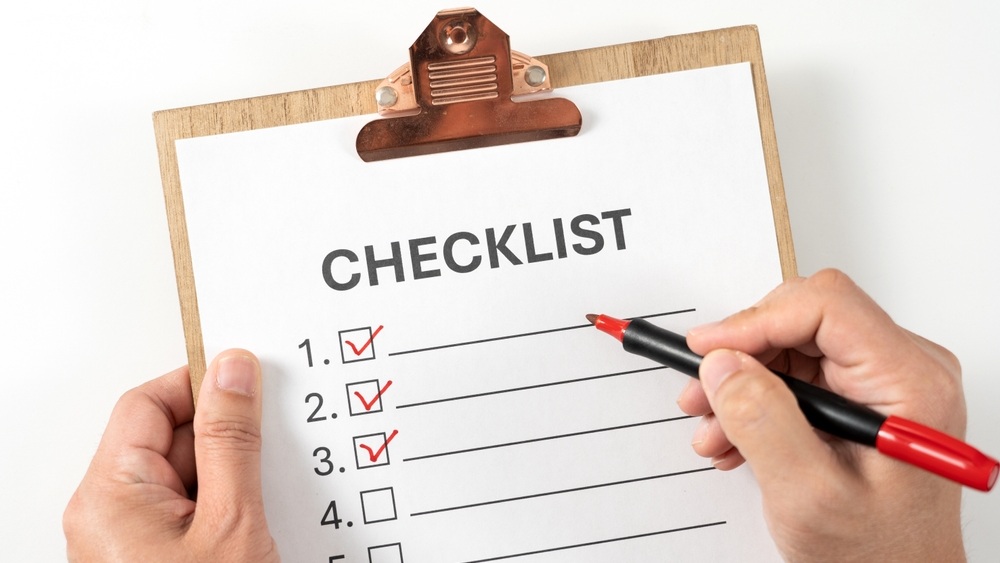 Checklist on the wooden clipboard, hands using a red marker pen to check off items on a white checklist