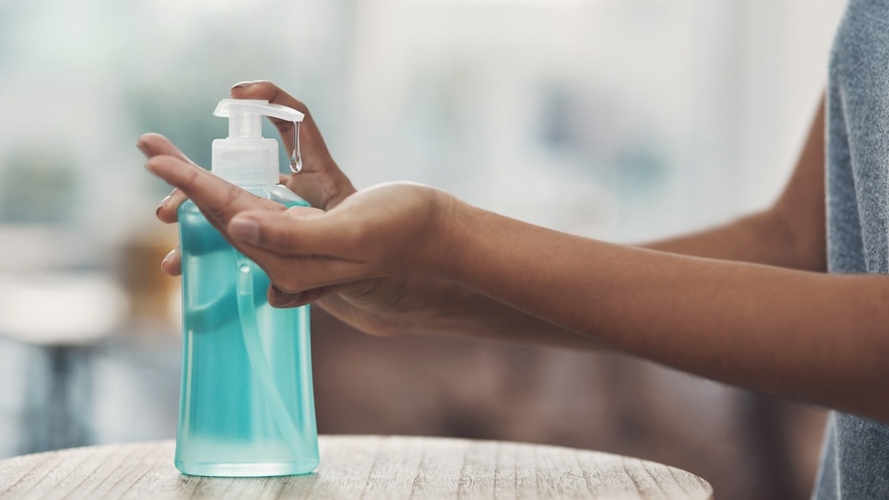 Person, hands and sanitizer with dispenser for drop of hygiene, cleaning gel or disinfection at home. Closeup, alcohol or liquid soap with protection for handwash, bacteria or germ removal at house