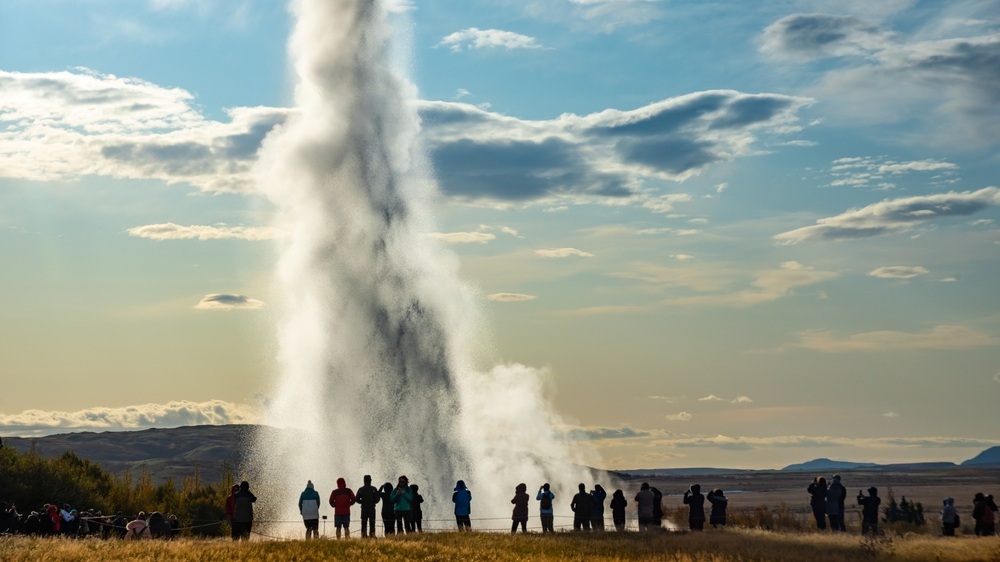 A dramatic geyser Strokkur eruption captured with a crowd of onlookers enjoying the impressive natural display. Golden Circle attraction.