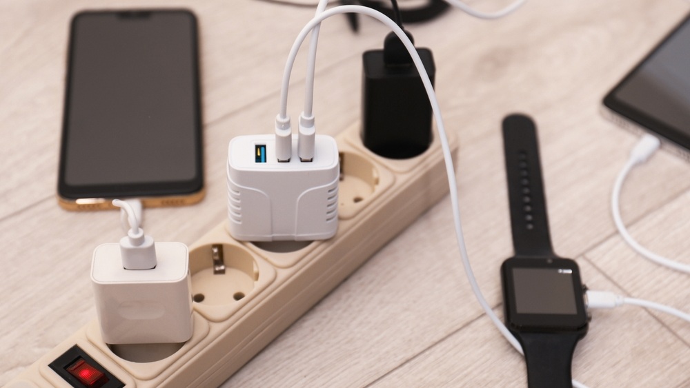 USB adapters with cables plugged into power strip charging devices on wooden floor, closeup