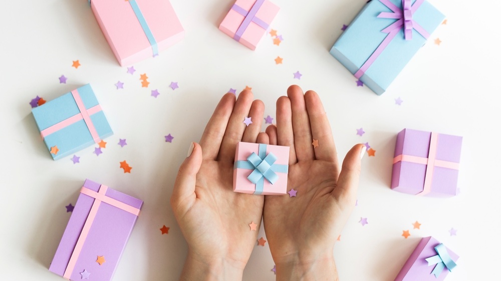 Hands holding a small pastel gift box. Pastel gift boxes with bows scattered around. Star confetti adds a festive touch. Perfect for celebrations and gifts. New year celebration image.