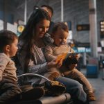Young Mother Sits in Departure Lounge, Holding Baby and Showing Travel Documents to Older Son. Family Travel, Parenting Challenges During Trips, Anticipation Holiday Flight at International Airport.