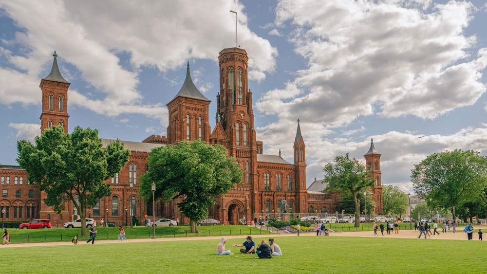 Washington D.C., USA - May 23, 2025. People relax on the lawn in front of the historic Smithsonian Institution Building on a partly cloudy day.