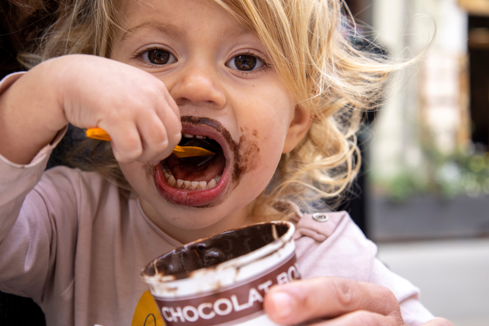 A small infant girl enjoys a chocolate icecream making a sticky mess on her face