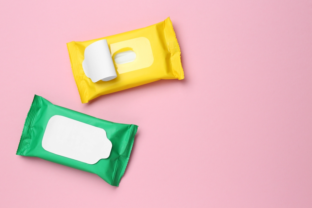 Wet wipes flow packs on pink background, flat lay. Space for text