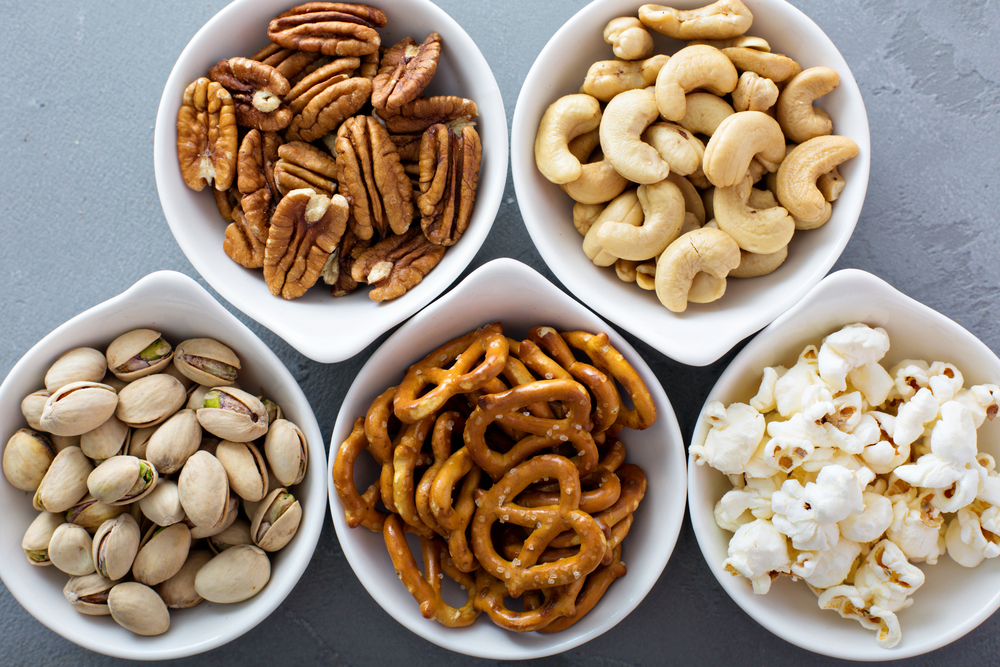 Variety of healthy snacks in white bowls pretzels and nuts