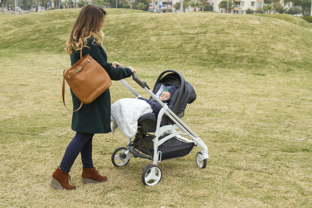 Happy young mother walking with baby stroller outdoors on the nature